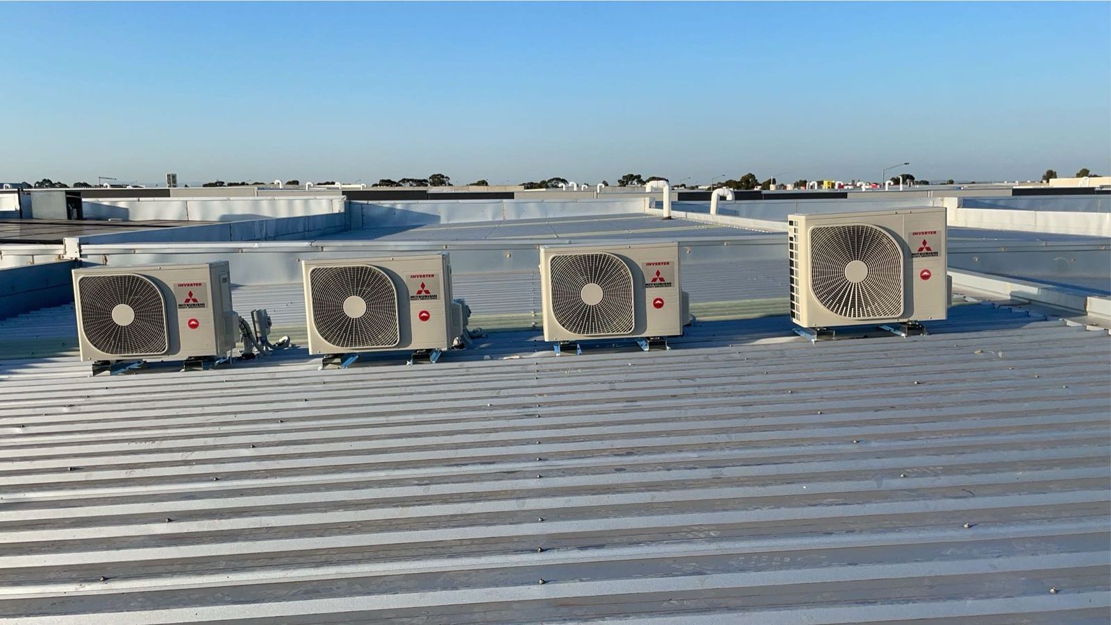 Four outdoor air conditioning units in a row on a commercial metal roof