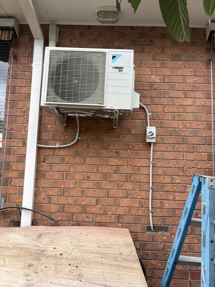 Daikin outdoor unit mounted on a brick wall with a ladder beside it
