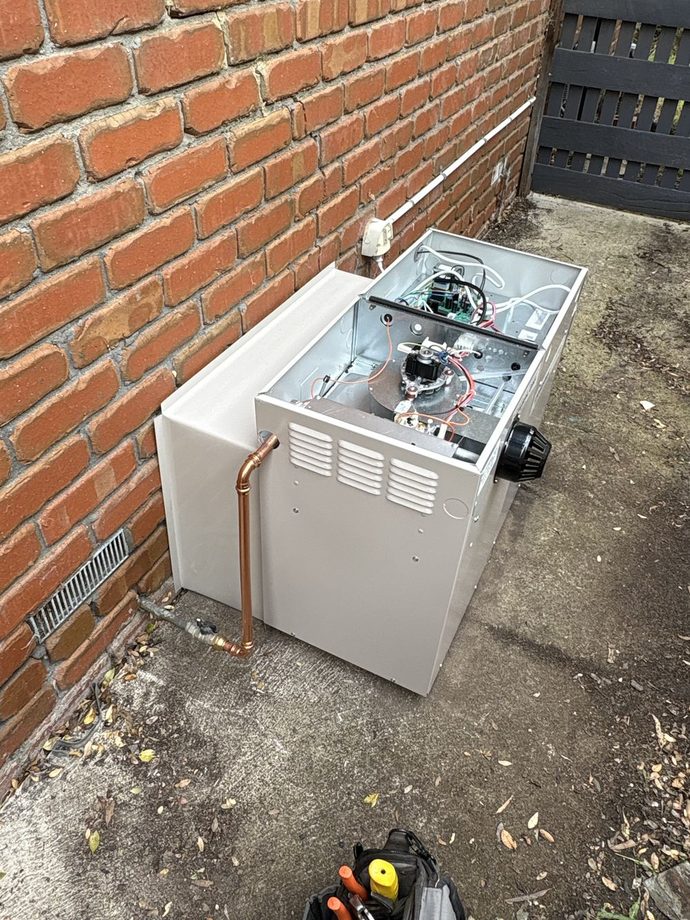 Ducted gas heater against a brick wall with its front panel off during the install