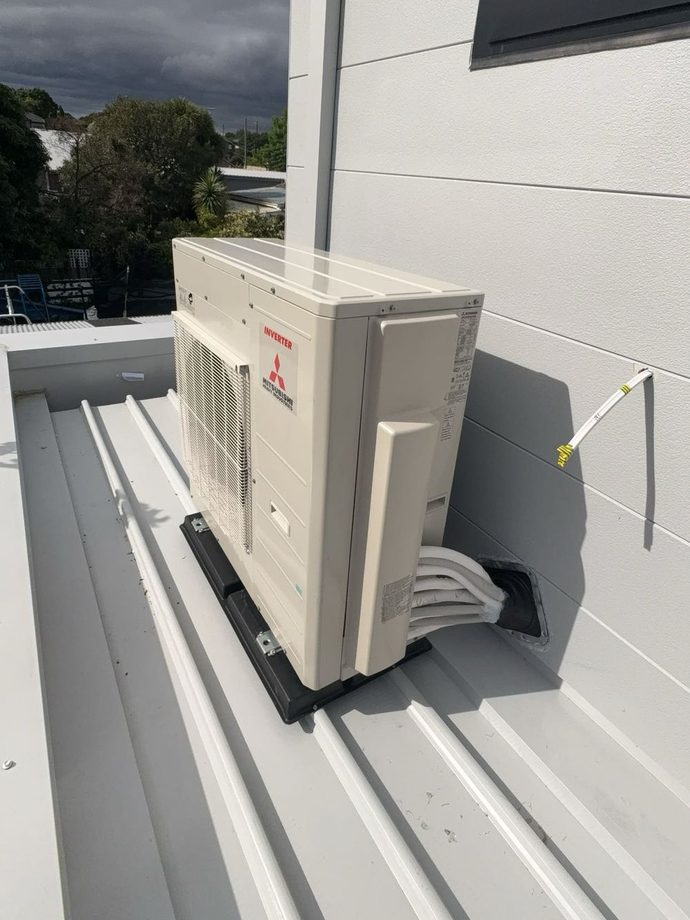 Outdoor air conditioning unit mounted on a roof beside a grey clad wall