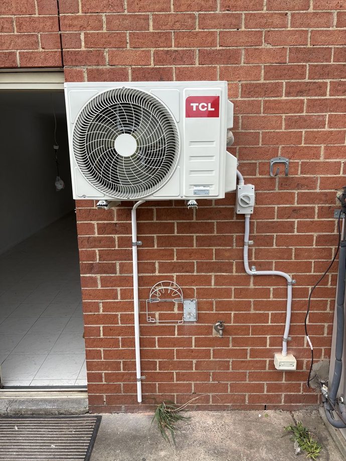 TCL split system outdoor unit on a brick wall with the pipes run in white conduit